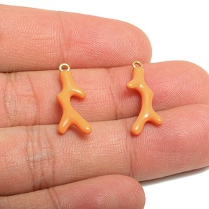 May include: Two coral-shaped charms in a light orange color with gold-colored loops. These charms are likely for jewelry making or crafting. The charms are shown against a neutral background.