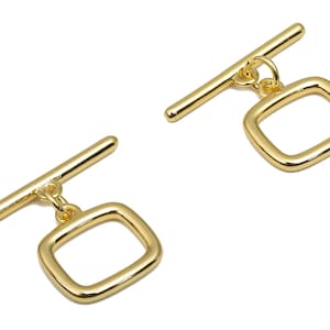 May include: Two gold-colored jewelry clasps. Each clasp has a rectangular loop pendant hanging from a horizontal bar. The clasps are made of shiny metal and are set against a white background. These clasps are used for necklaces and bracelets.