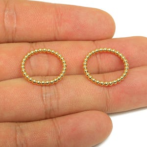 May include: Two gold-colored beaded rings are displayed against a skin-toned background. The rings are circular, with small, evenly spaced beads forming their structure. The rings are likely jewelry components or decorative elements.