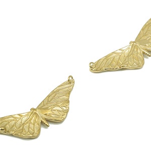 以下が含まれることがあります： 複雑な羽根のディテールを持つ、ゴールドトーンの金属製の蝶のチャームが2つ。チャームは、ジュエリーやその他のクラフトに取り付けるためのループが上部に付いています。