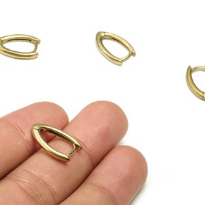 Può includere: Orecchini a cerchio ovali color oro. Gli orecchini hanno un design semplice e minimalista con chiusura a cerniera. Diversi orecchini sono sparsi su sfondo bianco.