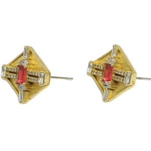 May include: A pair of gold earrings with a square design. Each earring features a red rectangular stone surrounded by smaller clear stones.
