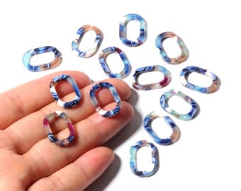 May include: Oval-shaped resin links in shades of blue, white, and brown. The links have a marbled appearance and are scattered on a white surface. Some links are held in a hand. These links are suitable for jewelry making.