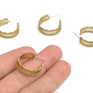 May include: Gold-colored hoop earrings with a decorative openwork design. The earrings have a post closure and a scalloped edge. Several earrings are visible against a white background.
