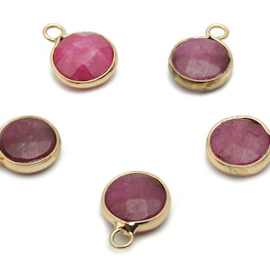 May include: Five gold-toned pendants with round pink gemstone cabochons. Each pendant has a small loop at the top for attaching to a chain or cord.