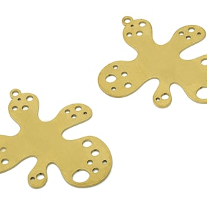 Puede incluir: Dos abalorios de metal de color dorado con forma de manchas abstractas con múltiples agujeros. Los abalorios tienen un acabado liso y brillante.