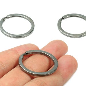 以下が含まれることがあります： 3つのシルバーカラーのキーリング。1つのキーリングは手で持ち、他の2つは別々に表示されています。キーリングは、キーを取り付けるためのスプリットを備えた円形です。金属はマット仕上げです。