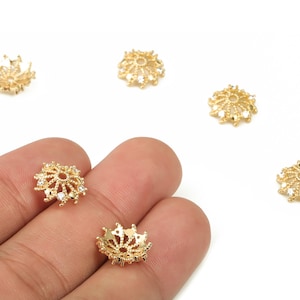 Könnte beinhalten: Nahaufnahme von mehreren goldfarbenen Perlenkappen im Filigranstil mit kleinen, klaren Kristallen. Die Perlenkappen sind auf weißem Hintergrund angeordnet, einige werden in einer Hand gehalten. Diese dekorativen Komponenten werden in der Schmuckherstellung verwendet.