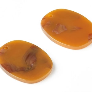 Puede incluir: Dos colgantes ovalados de resina marrón con un patrón de remolino y un agujero en la parte superior para colgar.