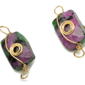 May include: Two green and pink gemstone pendants with gold wire wrapped around them. The wire is twisted into a spiral shape.