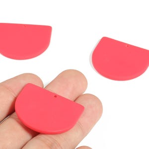 May include: Three bright red, semi-circular pendants with a small hole for stringing. The pendants are smooth and flat, and appear to be made of a solid material. These pendants are likely for jewellery making.