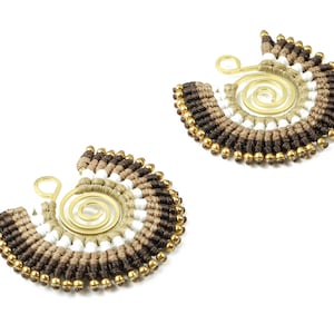 May include: A pair of brown, beige, and white beaded earrings with a gold spiral wire accent. The earrings are handmade and have a bohemian style.