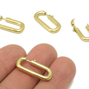 May include: Gold-colored, rectangular hoop earrings. The earrings have a simple, modern design with a hinged closure. Several earrings are displayed on a white background, with one held in a hand.