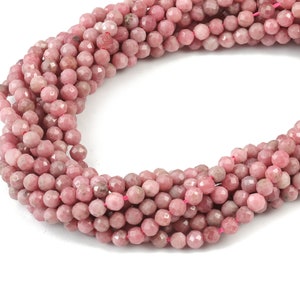 May include: A strand of pink gemstone beads, each bead is faceted and has a round shape.