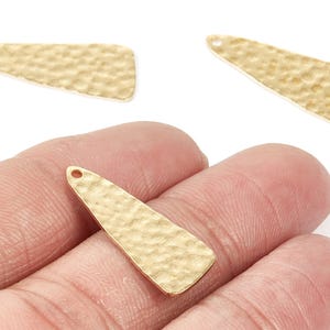 May include: Gold-colored, hammered metal pendant charms. The charms have a textured surface and a small hole at the top for stringing. The charms are teardrop-shaped and are suitable for jewelry making.