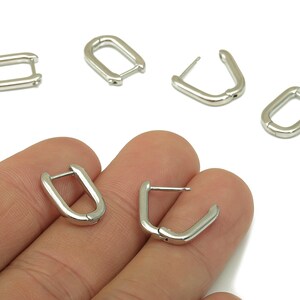 May include: Silver-colored, small hoop earrings. The earrings are in a U-shape with a post and clasp closure. Several earrings are displayed, some open and some closed. The earrings are on a white background.