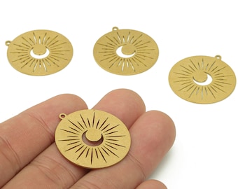 May include: Four gold-colored, circular pendants with a sunburst design and a crescent moon cutout. The pendants have a small loop at the top for attaching to jewelry. The pendants are held in a hand against a white background.