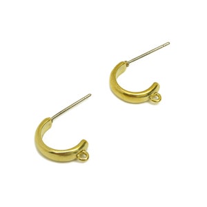 Pode incluir: Um par de brincos de argola dourados com um pequeno laço na parte inferior de cada argola. As argolas são de metal e têm um acabamento liso.