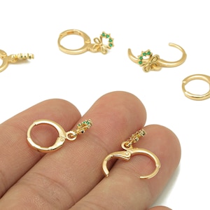May include: Gold-colored hoop earrings with a floral design and small green gemstones. The earrings are shown in a close-up view, with some of them open and some closed. The earrings are on a white background.