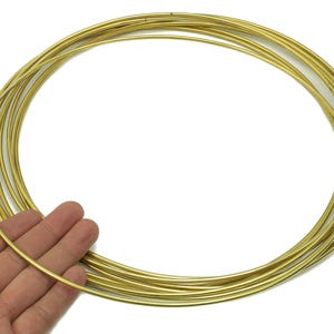 May include: A collection of thin, gold-colored metal rings, likely for jewelry making or crafts. The rings are held in a person's hand, showcasing their circular shape and metallic sheen. The rings appear to be approximately 0.08 inches in diameter.