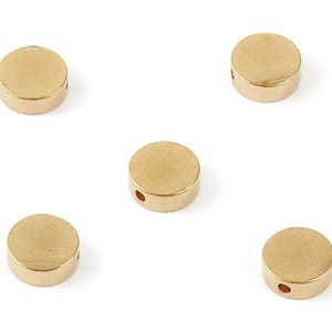 May include: Five gold-colored metal round beads with a hole in the center. The beads are smooth and have a slightly textured surface.