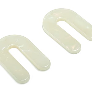 Könnte beinhalten: Zwei weiße U-förmige Kunststoff-Unterlegscheiben. Die Unterlegscheiben sind glatt und haben eine leicht irisierende Oberfläche.