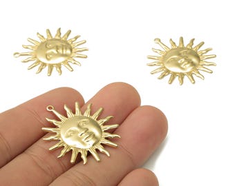 May include: Gold-colored sun charms with a smiling face and radiating rays. The charms have a small loop at the top for attaching to jewelry. The image shows three sun charms, one held in a hand.