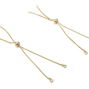 Puede incluir: Dos pulseras de cadena dorada con cuentas deslizantes ajustables y detalles de cristal transparente.