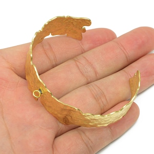 May include: A gold-colored cuff bracelet with a textured, organic design. The open-ended bracelet has a hammered appearance and a clasp. The bracelet is approximately 2.5 inches in diameter.