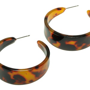 May include: A pair of large hoop earrings with a tortoiseshell pattern. The earrings are made of a thick, glossy plastic.