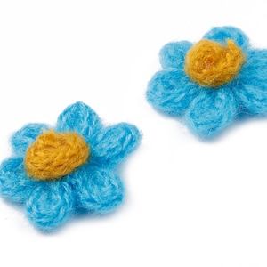 May include: Two blue felt flower embellishments with yellow centers. The flowers are handmade and have a fuzzy texture.