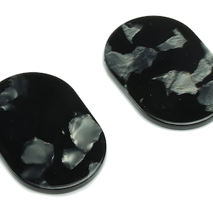 Puede incluir: Dos pendientes ovalados de resina negra con un patrón de mármol blanco.