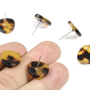 May include: A collection of tortoiseshell-patterned stud earrings. The earrings have a rounded triangular shape with a post for piercing. The earrings are a mix of brown and yellow tones.