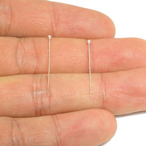 May include: Two delicate, straight, silver-colored pins, each with a small, round, silver bead at the top. The pins are displayed against a neutral background.