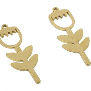 Puede incluir: Dos colgantes en forma de flor de color latón. Cada colgante presenta una flor estilizada con un diseño recortado y tres hojas en el tallo. Los colgantes tienen un pequeño lazo en la parte superior para colgar.