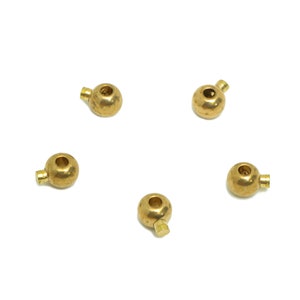 Może przedstawiać: Pięć złotych metalowych koralików z małą pętelką na każdym koraliku. Koraliki są ułożone w kształt gwiazdy na białym tle.