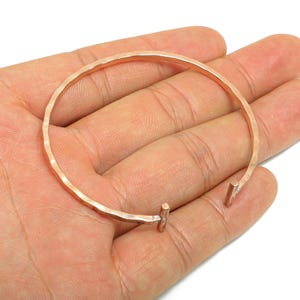 Op de afbeelding: Een gehamerde koperen manchetarmband. De open armband heeft een getextureerd oppervlak en een eenvoudig, minimalistisch ontwerp. De armband heeft een diameter van ongeveer 6,35 cm.