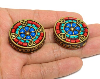 Könnte beinhalten: Zwei runde, dekorative Ohrringe mit Mosaikdesign. Die Ohrringe haben eine zentrale blaue Blume, umgeben von türkisfarbenen und roten Segmenten, mit goldfarbenen Akzenten und einem dunkelbraunen Rand.