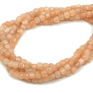 May include: A strand of peach-colored sunstone beads, each bead is faceted and has a square shape.