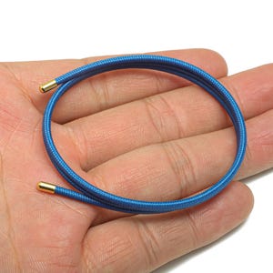 Könnte beinhalten: Eine aufgerollte blaue Kordel mit goldfarbenen Metallspitzen. Die Kordel ist ein leuchtendes Blau und scheint aus einem gewebten Material zu bestehen. Die goldenen Spitzen verleihen dem schlichten Design einen Hauch von Eleganz.