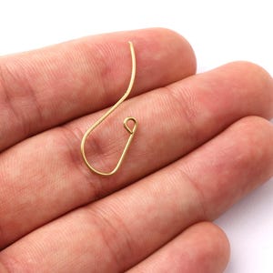 May include: A single gold-colored earring hook, crafted from wire, is displayed against a neutral background. The hook features a curved design with a looped end, showcasing a minimalist aesthetic. The earring hook is a jewelry component.