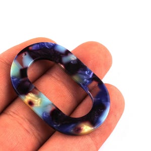 Peut inclure: Un pendentif ovale avec un motif marbré dans les tons de bleu, violet et jaune. Il comporte un trou pour l'enfilage. Ce composant de bijouterie convient aux colliers et aux boucles d'oreilles. Mesure environ 4 cm de long.