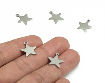 Puede incluir: Abalorios plateados en forma de estrella con un pequeño lazo en la parte superior para la fabricación de joyas. Los abalorios se muestran en una mano sobre un fondo blanco. Ideales para crear collares, pulseras y pendientes.