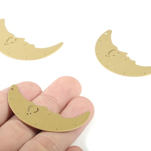 May include: Gold-colored crescent moon charms with a smiling face design. The charms have a small hole at the top for stringing. The moon charms are made of metal and are suitable for jewelry making or other craft projects.