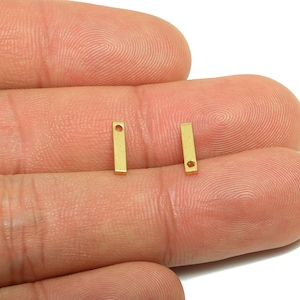 May include: Two small, rectangular gold-colored metal charms with a single hole at the top and a smaller hole near the bottom. The charms are shown against a neutral background.