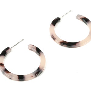 May include: A pair of hoop earrings with a tortoiseshell pattern. The earrings are made of a white and black material and have a silver post.