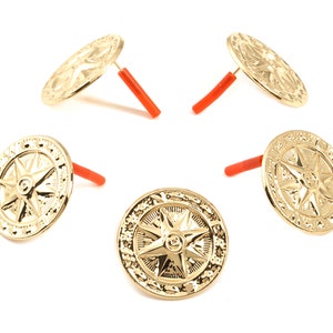 Puede incluir: Cinco adornos de metal de color dorado con un diseño de estrella y un tallo de plástico rojo. Los adornos están dispuestos en círculo sobre un fondo blanco.