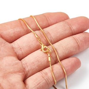 Könnte beinhalten: Eine goldene Kettenkette mit einem Karabinerverschluss. Die Kette ist dünn und zart.