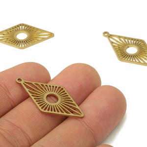 Könnte beinhalten: Drei goldfarbene, rautenförmige Metallanhänger mit Sonnenstrahlendesign. Jeder Anhänger hat oben eine kleine Schlaufe zum Befestigen an Schmuck. Die Anhänger werden vor weißem Hintergrund gezeigt.