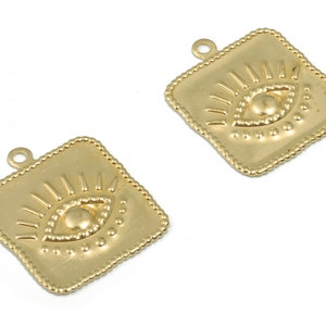 May include: Two gold-toned metal charms in the shape of a square with a raised evil eye design. The eye is surrounded by a circle of small dots and has a raised pupil.